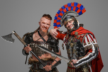 Joyful viking and roman soldier posing against gray background