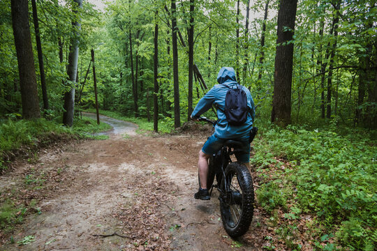 A man on an electric bike with thick wheels rides through a wet forest. Cool sports hobby.