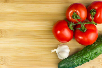 Red tomatoes, green cucumber, garlic on a wooden board