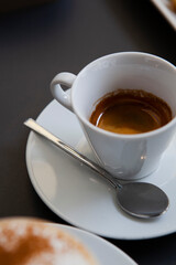 Traditional Italian breakfast. Small white ceramic cups with espresso (coffee) on a table with a saucer and a metal spoon at a local bar (coffee shop) in Milan, Lombardy, Italy. European drinks.