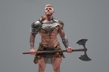 Handsome northern warrior holding axe against gray background