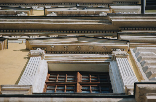 Window on the facade of a house with beige plaster in the central historical part of the city. Beautiful decorative architecture with reliefs, cornice and white columns in Lviv, Ukraine. Bottom view.