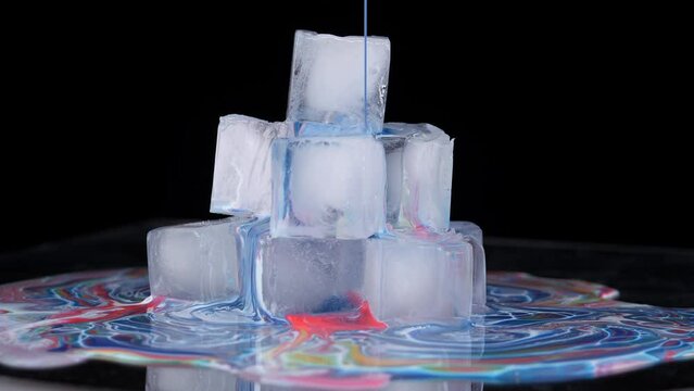 Multi-colored paint spreads over the surface of the ice cubes and flows down onto the plane.