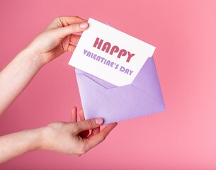 Hands putting card with happy Valentines day greeting in envelope. Celebration postcard on pink background. High quality photo
