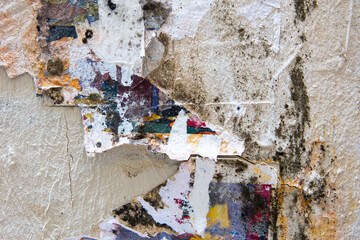 Peeling wall background, dirty and with remains of posters and paint. Different colors. Urban background.