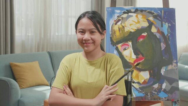 Asian Artist Girl In Wheelchair Holding Paintbrush And Cross His Arms And Smile While Painting On The Canvas
