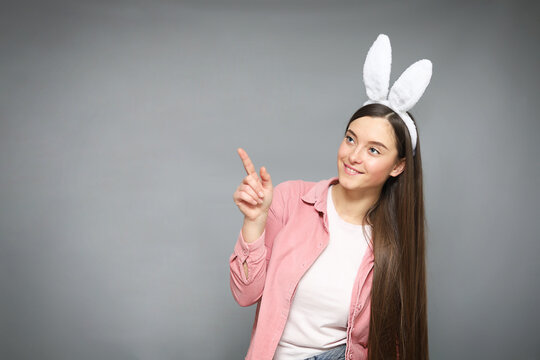 Attractive and smiling young girl with bunny ears pointing Picture taken in  grey background with copy space