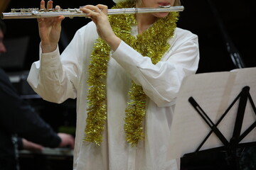 A person playing a flute on notes with celebratory tinsel on clothes