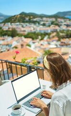Rear view freelancer woman working on laptop computer with white empty screen over Mediterranean view from outside balcony travel hotel - 485397969