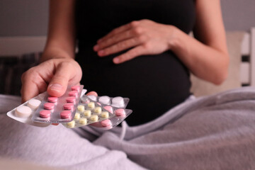 a pregnant woman holds vitamins and pills in her hand against the background of her belly