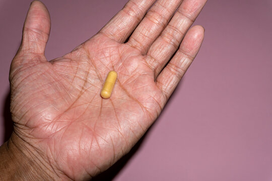 Close up picture of a man hand holding ginger root capsules. Treating nausea and vomiting after surgery, dizziness, menstrual pain, arthritis, preventing morning sickness.