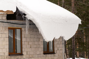 A sheet of snow hangs from the roof of a house.