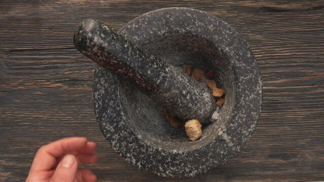 Top view of hands putting sea salt and brown sugar into the grey stone mortar