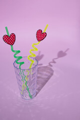 A glass with love straws for two on a pink background. All this creates a shadow.