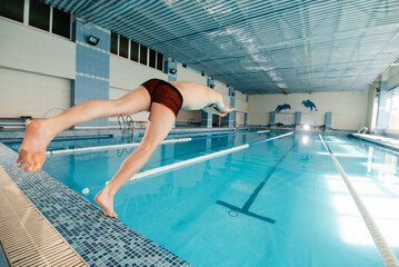 A young man dives and jumps into the water of a modern swimming pool. Training and sports development. Preparation for competitions, and a healthy lifestyle. Water treatments and a healthy lifestyle.
