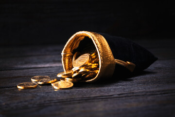 A bag with gold coins on a wooden background. The money is in a black bag. Treasure Hunt