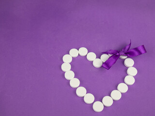 Heart made of white pills on a purple background.