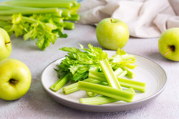 Sliced fresh celery stalk with leaves on a plate and green apples on the table ready to be cooked. Vegetarian food