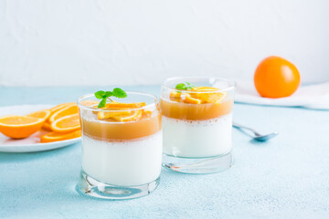 Panna cotta with orange and mint leaf in glasses on a light table. Sweet Italian dessert