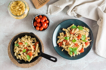 A plate of pasta with tomatoes and basil on a plate and cooking ingredients on the table. Mediterranean cuisine. Top view