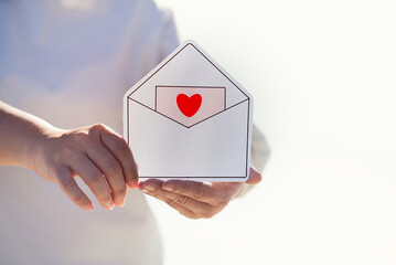 Woman's hands holding paper cut of heart in envelope, encouragement, world mental health day,sharing,organ or heart donation, 14 February valentine, Love and sending email, dating singles concept.