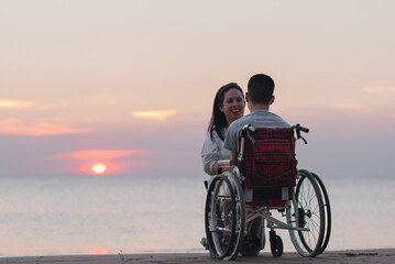 Behind of young man with disability and parent or volunteer or caregiver looking sunset on the sea...