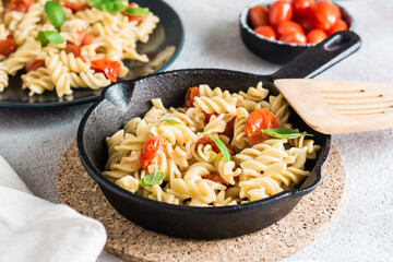 Pasta with tomatoes and basil in a pan and in a plate and a bowl with tomatoes on the table. Mediterranean cuisine.