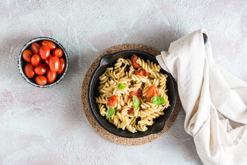 Pasta with tomatoes and basil in a pan and in a plate and a bowl with tomatoes on the table. Mediterranean cuisine.  Top view