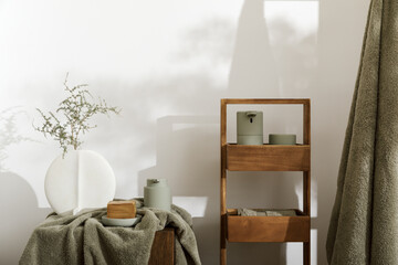 Modern aesthetic bathroom accessories in eucalyptus green shade. Organic cotton bath towels, minimalistic white  vase, sensor soap and lotion dispenser  on solid oak stump. Daily body care concept