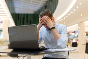 Feeling tired. Frustrated young man covering his face with hands while working on laptop