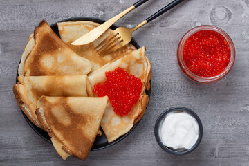 Russian pancakes with red caviar on a grey table