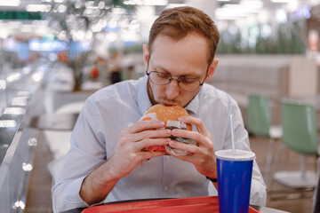 Office worker eating fast food burger and drink soda at food court in mall at lunch