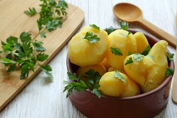 Cocked potatoes in brown clay bowl at the table, decorated with fresh green parsley