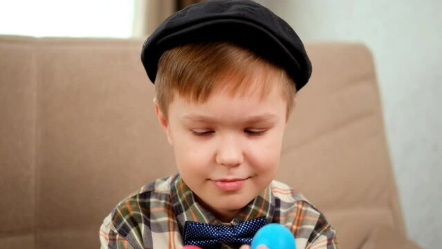 A blond caucasian boy in a cap closes his eyes with Easter eggs and plays with them
