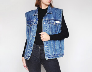 Young woman wearing a vintage oversized denim vest, black turtleneck and black jeans isolated on white background. Copy space
