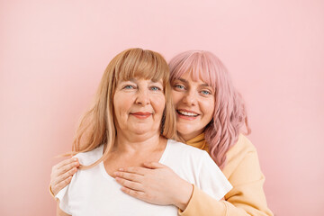 Beautiful family of senior mother and daughter smiling and hugging together on pink pastel wall.
