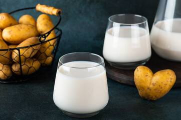 Pouring vegan potato milk in glass and potato in bowl on dark background. Vegan milk. Plant based milk replacer and lactose free. Vegetable milk