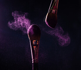 Make-up brushes with pink or violet powder explosion on dark background