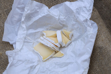 Sliced cheese with white camembert mold in an unwrapped package on burlap