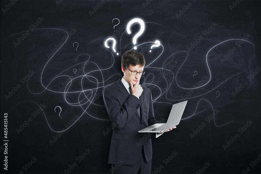 Poster attractive young european businessman with laptop standing on concrete background with question mark