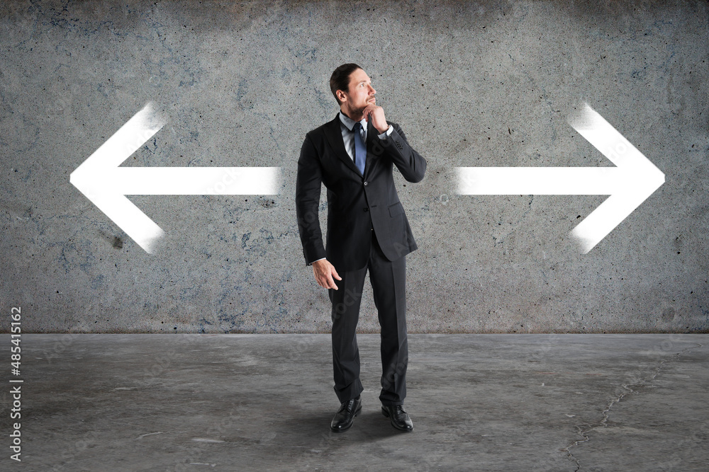 Poster thoughtful young businessman standing on abstract concrete background with two arrows. different dir