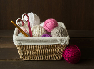 Fototapeta na wymiar colorful woolen balls with crochet hooks in a wooden basket in front of a dark brown wooden background