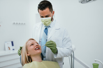 Beautiful young woman having dental treatment at dentist's office. Dentist is wearing protective...