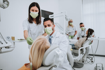 Beautiful young woman having dental treatment at dentist's office. Dentists are wearing protective face masks due to coronavirus pandemic..