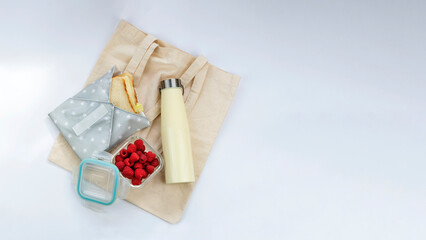 Reusable shopping bag, sandwich in reusable wrap, raspberries in glass container and metallic water bottle. Zero waste, sustainable living concept