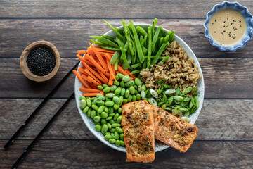 Top down view of an Asian salmon salad bowl with dressing and black sesame seeds