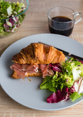 Still life with croissant with prosciutto and green salad and coffee. Healthy breakfast concept.