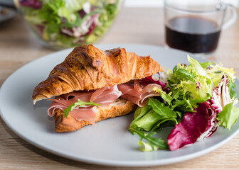 Still life with croissant with prosciutto and green salad and coffee. Healthy breakfast concept.