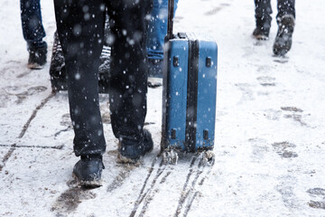 Tourists with suitcases walk along a snowy street in winter