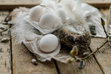 Easter natural eggs in tray, feathers, willow branches, nest, linen cloth on aged wooden table. Stylish Easter rustic still life. Simple rural aesthetics. Happy Easter